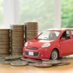 What Happens To Car Finance In An IVA red car over a lot of stacked coins showcasing what happens to car finance in an IVA